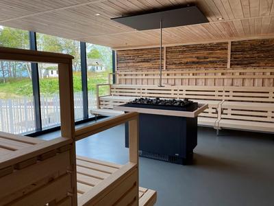 Moderner Saunaraum mit hellem Holz und großem Ofen in der Mitte.