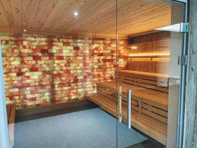 Sauna room with wooden panels, illuminated salt wall tiles, wooden benches, and glass door.