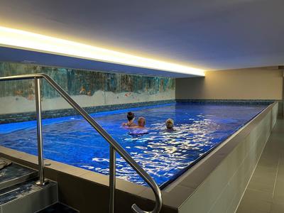 Indoor pool with stainless steel railing and two people swimming in clear water.