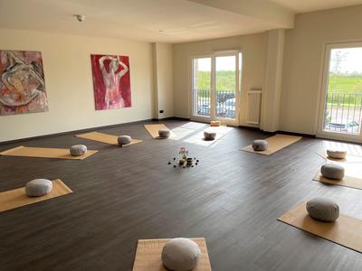 Heller Yogaraum mit Meditationskissen auf gelben Matten und großem Fenster mit Blick ins Grüne.