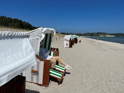 Strand mit weißen Strandkörben, blauem Himmel und weiter Sicht aufs Meer.