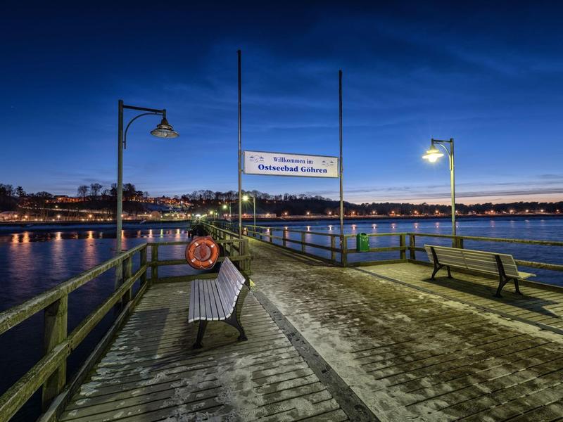 Evening view of a pier with benches and lampposts by the water under a clear sky.