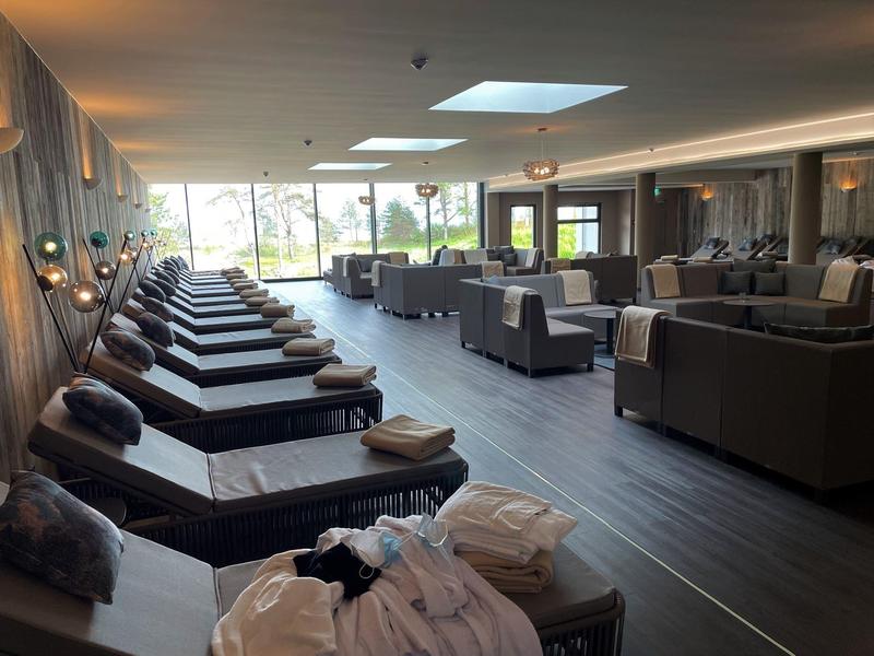 Modern spa room with loungers, cozy seating areas, large windows, and a calm atmosphere.