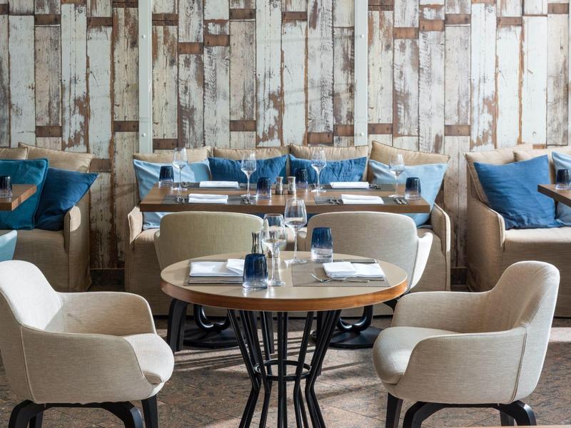 Modernes Restaurant mit runden Holztischen, gepolsterten Stühlen und rustikaler Holzvertäfelung.