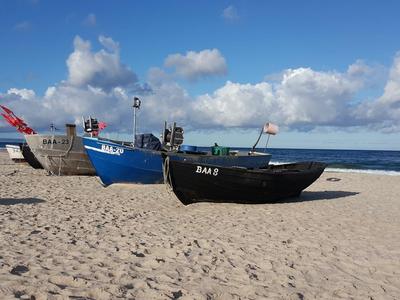 Fischerboote stehen auf sandigem Strand unter blauem Himmel mit weißen Wolken.