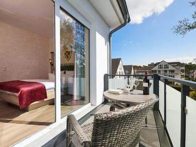 Balkon mit zwei Stühlen und Tisch, Glasgeländer, Blick auf Nachbarhäuser und blauer Himmel.