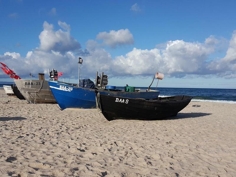 Fischerboote stehen auf sandigem Strand unter blauem Himmel mit weißen Wolken.