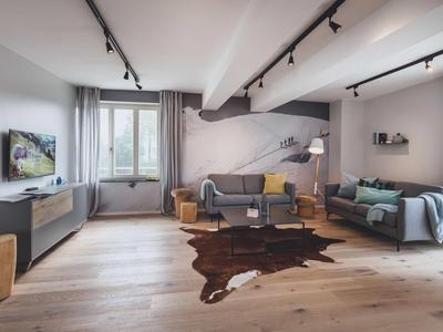 Soggiorno moderno con due divani, pavimento in legno, grande finestra, luminoso e accogliente.