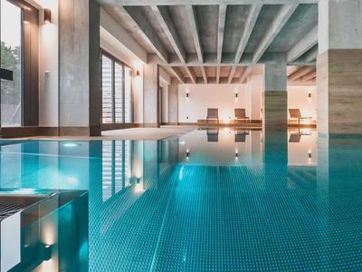 Piscina interna moderna con lettini e grandi finestre che lasciano entrare la luce naturale.