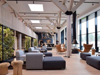 Moderne und helle Hotellobby mit großen Fenstern, bequemen Sitzbereichen und warmem Holzboden.