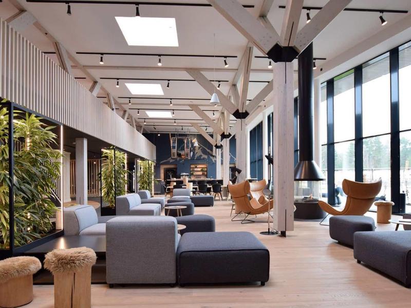 Hall d'hotel moderno e luminoso con grandi finestre, aree salotto confortevoli e pavimento in legno caldo.