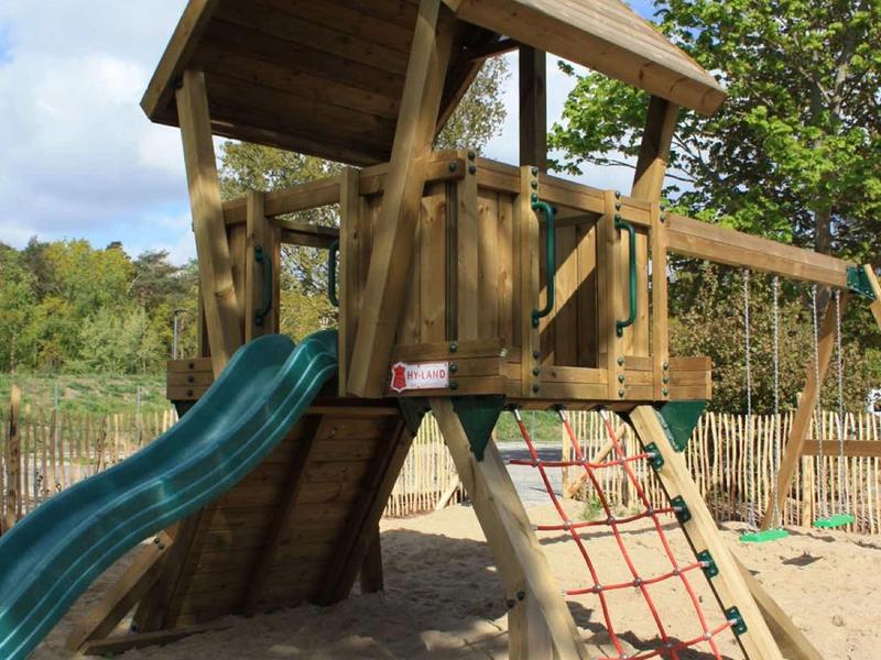 Parco giochi in legno con scivolo e struttura per arrampicarsi sulla sabbia sotto un cielo azzurro