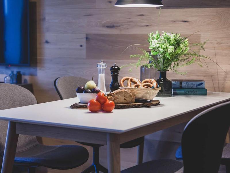 Tavolo da pranzo moderno con sedie, frutta e composizione floreale in una stanza accogliente.