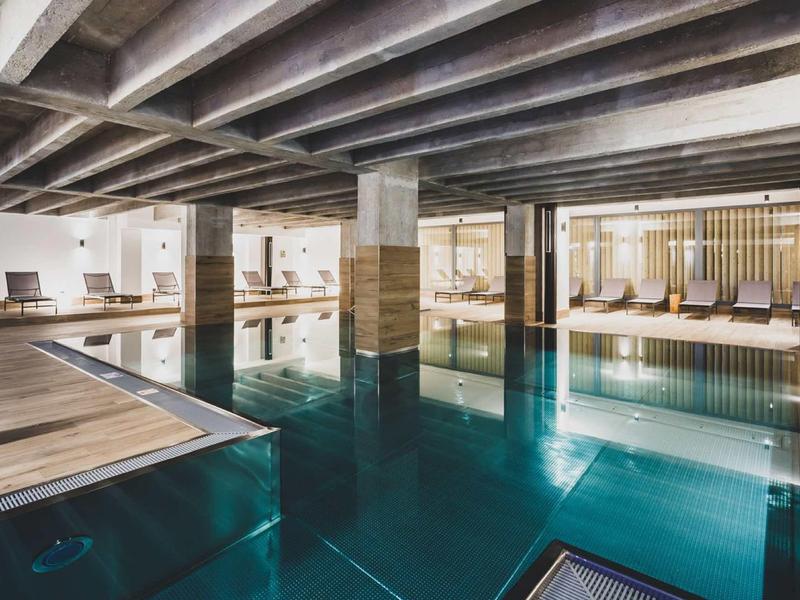 Piscina interna moderna con terrazza in legno e lettini in un hotel