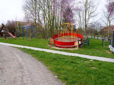 Aire de jeux pour enfants avec manège, bac à sable et structure d'escalade dans une prairie verte.