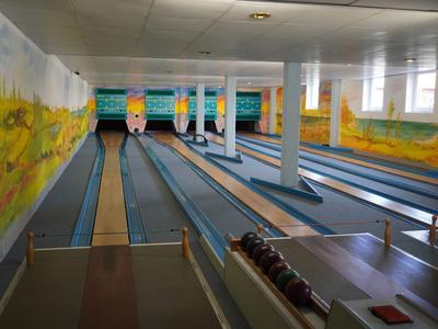 Vista interna di una pista da bowling con più corsie e murales colorati.