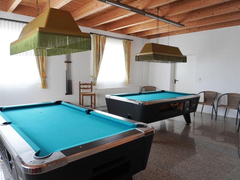 Salle de billard avec deux tables, lampes suspendues et chaises près du mur.