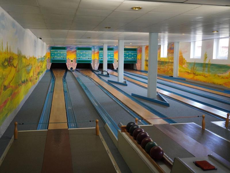 Allée de bowling avec plusieurs pistes et murs peints de paysages colorés.