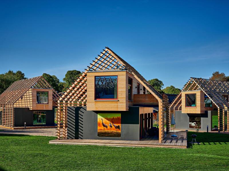 Moderne Holzhäuser mit großen Fenstern und offenem Dachstuhl unter blauem Himmel.