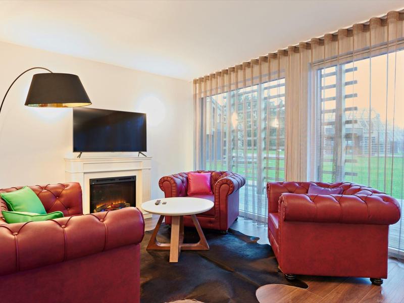 Gemütliches Wohnzimmer mit roten Sofas, großem Fenster, TV, Kamin und stehendem Lampenschirm.