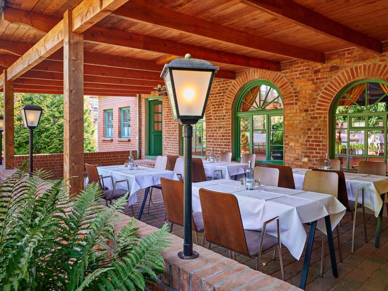 Überdachte Außenterrasse mit Holzdach, weißen Tischen, gepolsterten Stühlen und Laternenlampen.