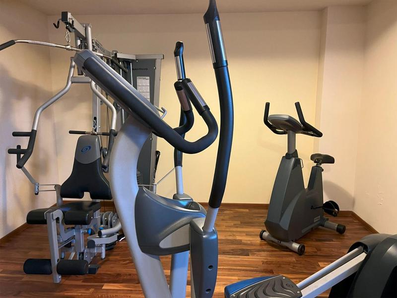 Kleiner Fitnessraum mit Ellipsentrainer, Heimtrainer und Kraftstation in hellen Wänden.