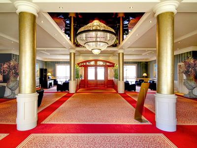 Eleganter Hotellobby mit roten Teppichen, goldenen Säulen und großem Kronleuchter.