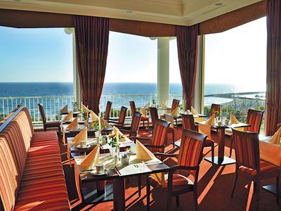 Elegant restaurant with sea view and red-striped chairs and tables.
