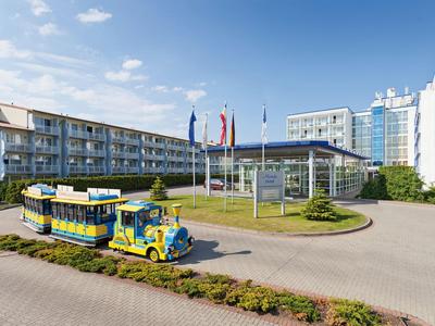 Colorato trenino davanti a un hotel moderno con bandiere e cielo azzurro.