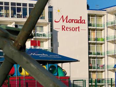 Außenansicht eines mehrstöckigen Resorts mit blauem Sonnenschirm und Spielplatzgeräten