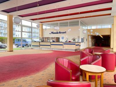 Interno di un hotel con poltrone rosse e reception sullo sfondo.