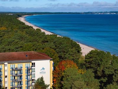 Hotel mit gelber Fassade neben bewaldetem Küstenstreifen und blauem Meer im Hintergrund