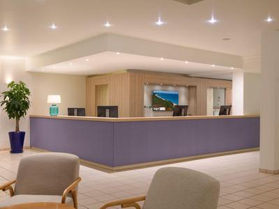 Moderne Hotelrezeption mit lila Tresen und bequemen Stühlen in hellem Raum.