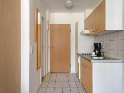 Schmale Küche mit weißen Fliesen und hölzernen Schränken in einem Hotelzimmer.