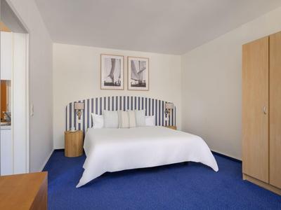 Ein schlicht eingerichtetes Schlafzimmer mit blauem Teppich, Doppelbett und Holzschrank.