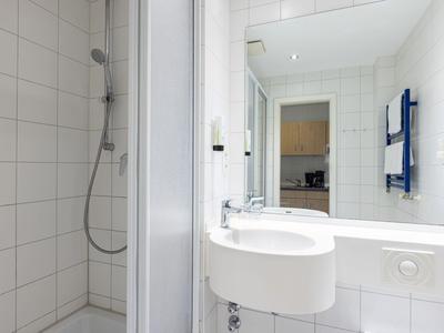 Kleine weiße Badezimmer mit Dusche, Waschbecken und großem Spiegel.