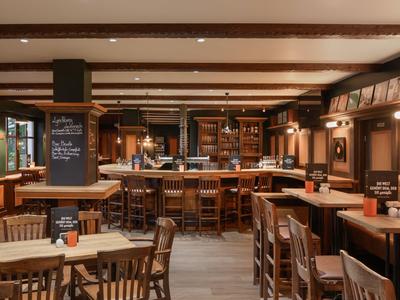 Gemütliche Hotelbar mit Holzstühlen, Tischen und einer langen Bar im Hintergrund.