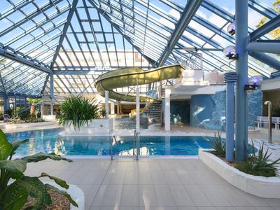 Moderner Innenpool mit Glasdach und Rutsche, dekoriert mit Pflanzen.