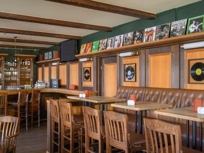 Gemütliche Bar mit Holzmöbeln, Lederbänken und Regal mit Schallplatten und Büchern.