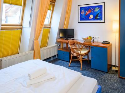 Cozy hotel room with double bed, desk, and chair in front of a window with yellow curtains.