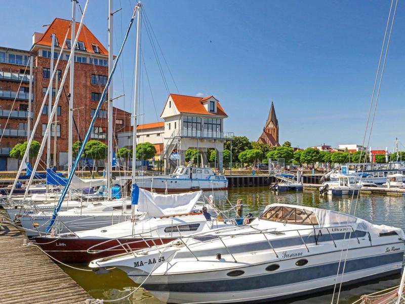 Segelboote im Hafen vor Gebäuden bei klarem Himmel und sonnigem Wetter.