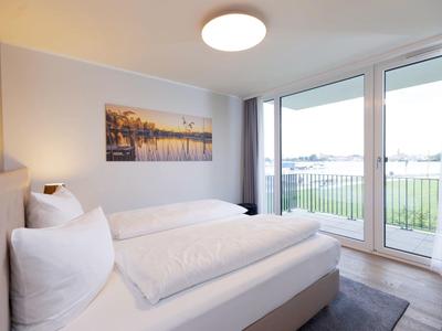 Bright hotel room with double bed, large window, and balcony overlooking greenery.