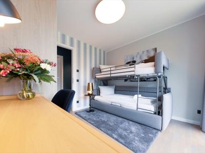 Modern hotel room with bunk bed, desk, and flower arrangement.
