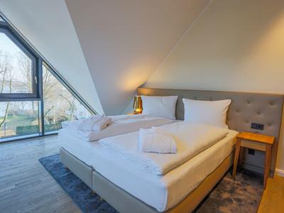 Modern hotel room with large bed, two towels, bedside lamps, and a triangular window.