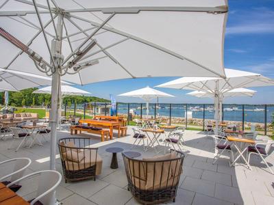 Terraza con zona de estar, mesas y sombrillas con vistas al mar bajo un cielo despejado.