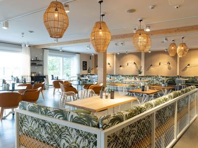 Restaurante moderno con muebles claros, patrones de plantas y lámparas colgantes de mimbre.