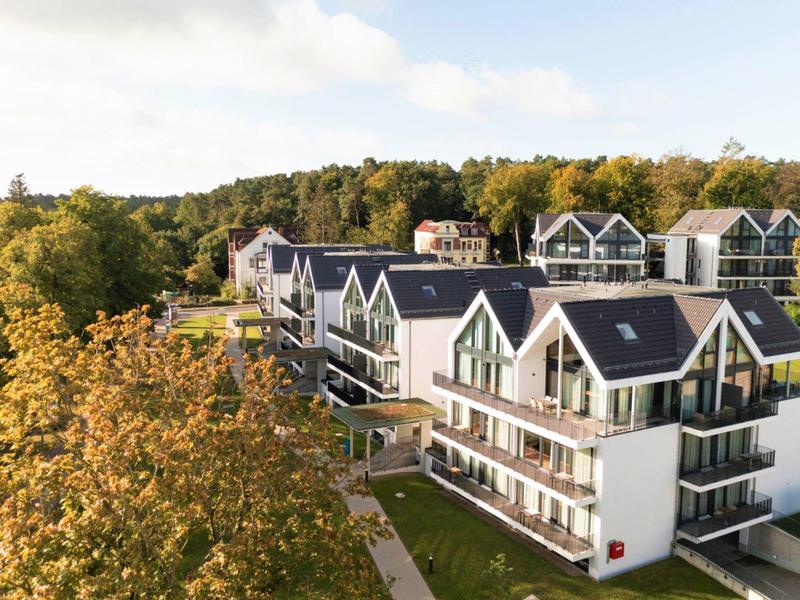 Modern hotel building with black roofs in a green, wooded area during daylight.