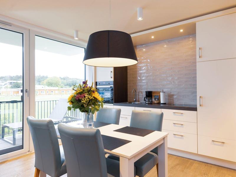 Bright modern kitchen with dining table, gray chairs, and large window to the terrace.