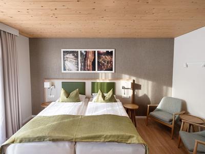 Modernes Schlafzimmer mit zwei getrennten Betten, grünen Akzenten und Holzmöbeln.