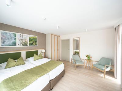 Helles Hotelzimmer mit zwei Betten, grün-weißer Bettwäsche und Sitzbereich mit Stühlen und Tisch.